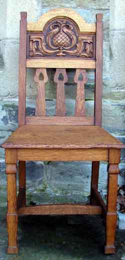 Oak hall chair with carved design of thistle and leaves, the heart pierced slats and chamfered legs are typical of Shapland and Petter design 